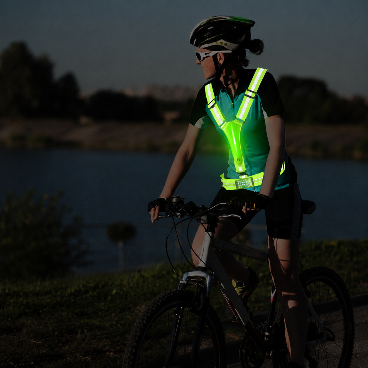 Female cyclist by lake wearing GlowStride LED safety vest at dusk